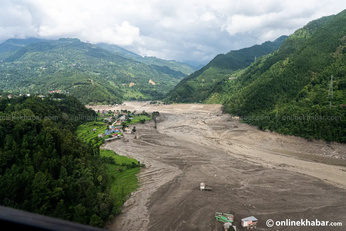 Aerial view of a settlement sitting at the edge of a wide new grey plain of flood deposits