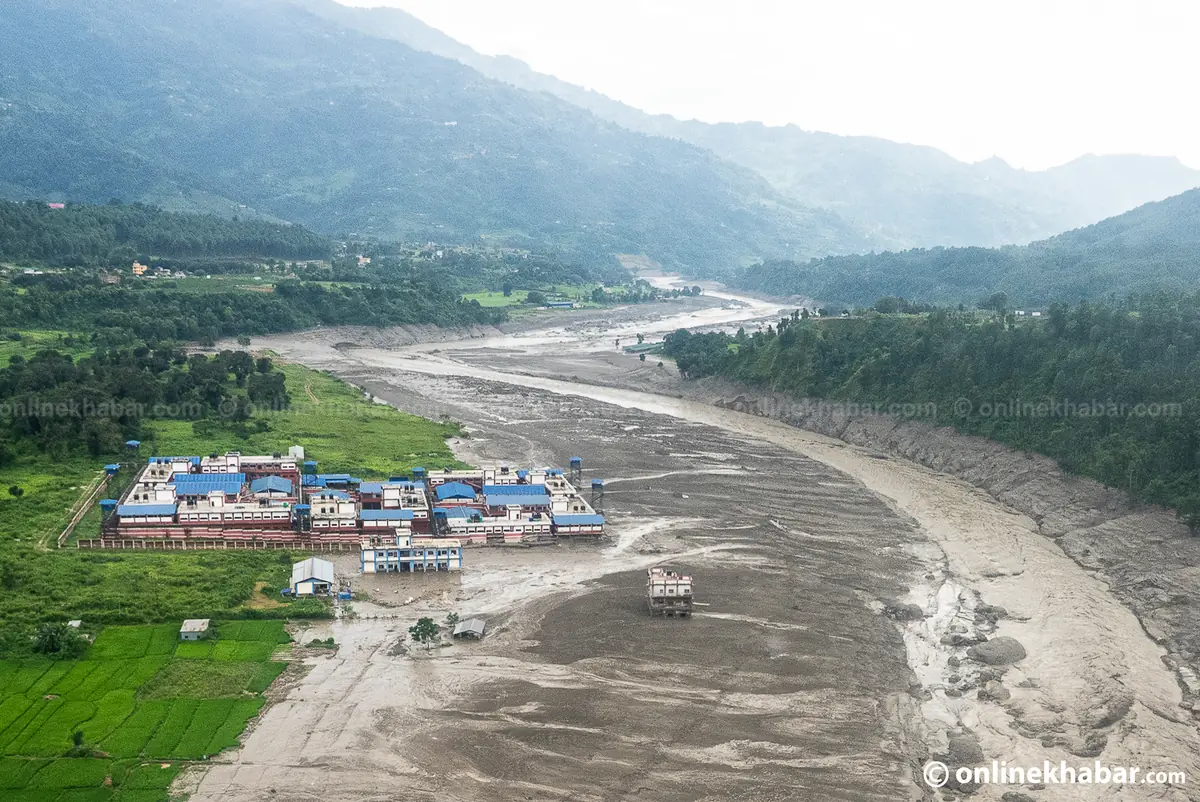 Aerial view of a riverside town with a helicopter overhead beside a river channel widened by the flood