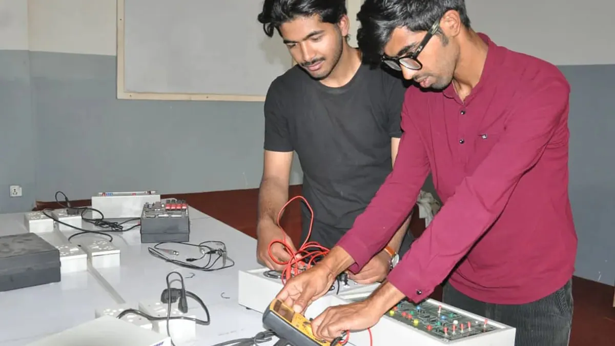 Two students probing a trainer board with a hand-held multimeter