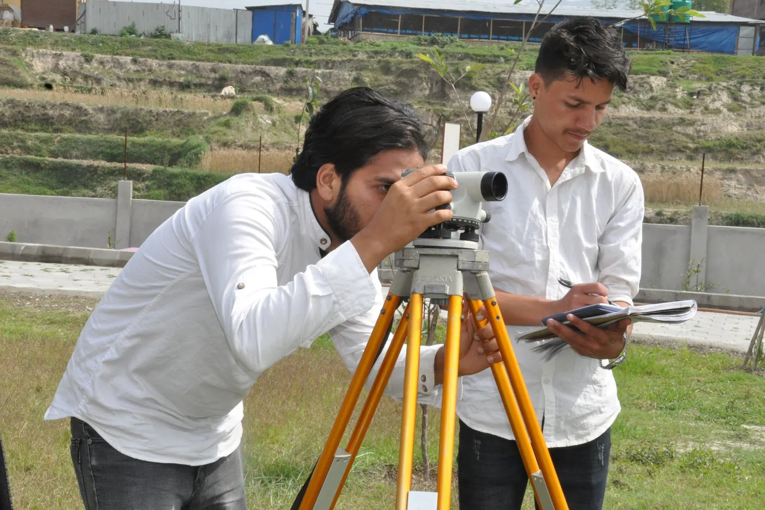Two students setting up a level on a tripod and writing down observations